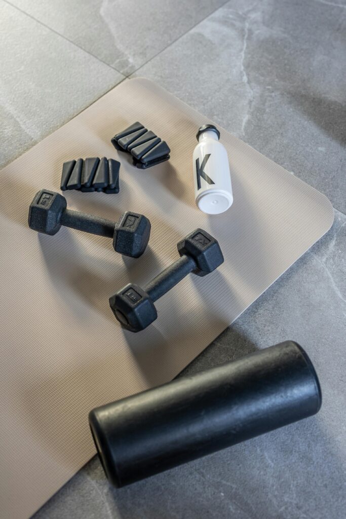 Flat lay of dumbbells, weights, and bottle on mat for fitness home workout.