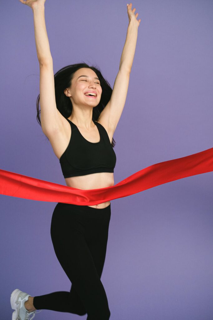 A joyful female athlete celebrates as she crosses the finish line, wearing activewear.